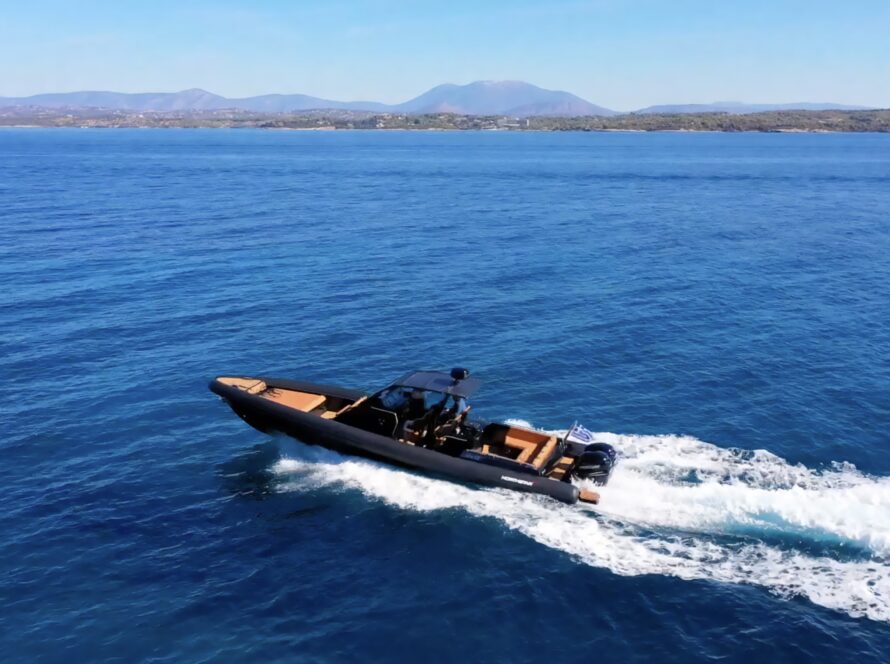 A speedboat cruising on open blue water with a distant shoreline and mountains in the background.