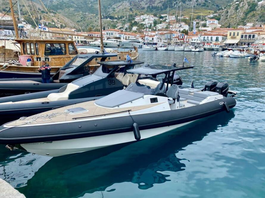 Several sleek and modern speedboats docked at a harbor with a picturesque town and mountainous landscape in the background.