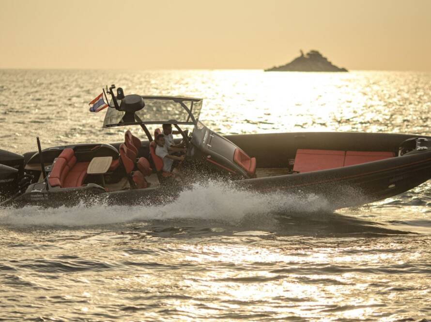 A speedboat with red seats cruising on the ocean at sunset with a small island in the background.