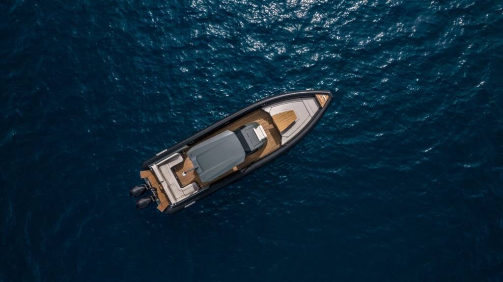 Top-down view of a luxury speedboat with cushioned seating and wooden decking, floating on deep blue water.